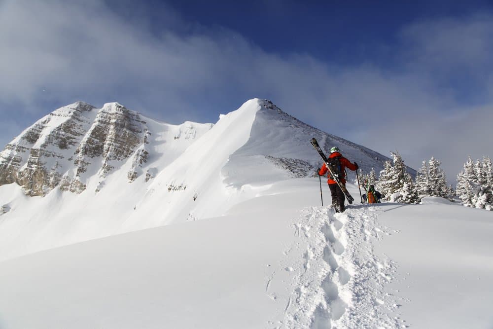 Backcountry skier bootpacking up a snowy ridge with skis on their back